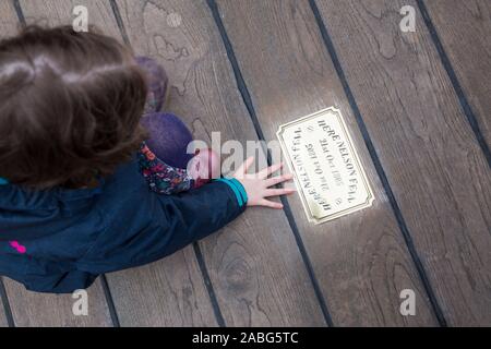 Kind Gast/kid Touristische untersuchen die Metall Messingschild auf der Website von HMS Victory an der Stelle, wo Admiral Lord Nelson fiel nach geschossen wird von einem französischen Musketier. Portsmouth. Großbritannien (105) Stockfoto