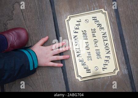 Kind Gast/kid Touristische untersuchen die Metall Messingschild auf der Website von HMS Victory an der Stelle, wo Admiral Lord Nelson fiel nach geschossen wird von einem französischen Musketier. Portsmouth. Großbritannien (105) Stockfoto