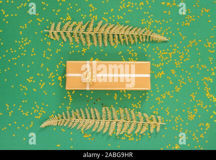Helle glänzende goldene Farnblätter und Geschenkboxen auf grünem Hintergrund mit Glitter gold Sterne, Flach, Ansicht von oben, kopieren Raum Stockfoto
