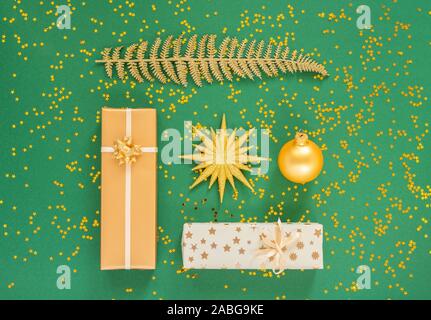 Helle glänzende goldene Farnblätter und Geschenkboxen mit Weihnachten Kugeln auf einem grünen Hintergrund mit Glitter gold Sterne, Flach, Ansicht von oben, kopieren Raum Stockfoto