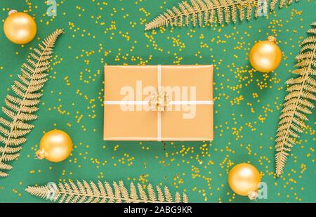 Helle glänzende goldene Farnblätter und Geschenkboxen mit Weihnachten Kugeln auf einem grünen Hintergrund mit Glitter gold Sterne, Flach, Ansicht von oben, kopieren Raum Stockfoto