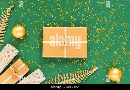 Helle glänzende goldene Farnblätter und Geschenkboxen mit Weihnachten Kugeln auf einem grünen Hintergrund mit Glitter gold Sterne, Flach, Ansicht von oben, kopieren Raum Stockfoto
