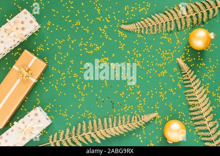Helle glänzende goldene Farnblätter und Geschenkboxen mit Weihnachten Kugeln auf einem grünen Hintergrund mit Glitter gold Sterne, Flach, Ansicht von oben, kopieren Raum Stockfoto