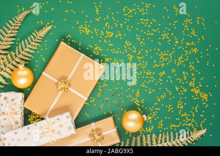 Helle glänzende goldene Farnblätter und Geschenkboxen mit Weihnachten Kugeln auf einem grünen Hintergrund mit Glitter gold Sterne, Flach, Ansicht von oben, kopieren Raum Stockfoto