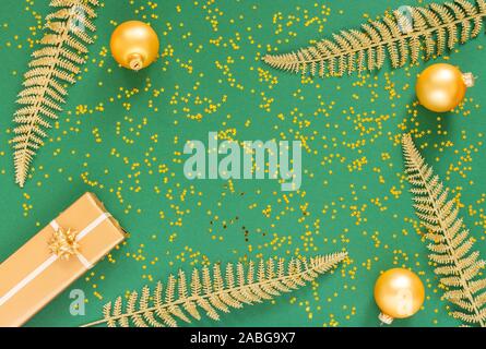 Helle glänzende goldene Farnblätter und Geschenkboxen mit Weihnachten Kugeln auf einem grünen Hintergrund mit Glitter gold Sterne, Flach, Ansicht von oben, kopieren Raum Stockfoto