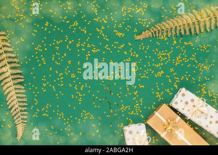 Helle glänzende goldene Farnblätter und Geschenkboxen auf grünem Hintergrund mit Glitter gold Sterne, Flach, Ansicht von oben, kopieren Raum Stockfoto