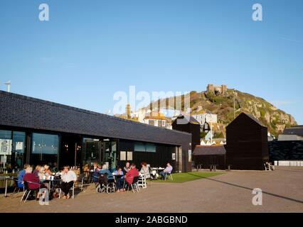 Menschen außerhalb der Stade Cafe/Restaurant am Meer in Hastings mit East Hill im Hintergrund sitzen Stockfoto