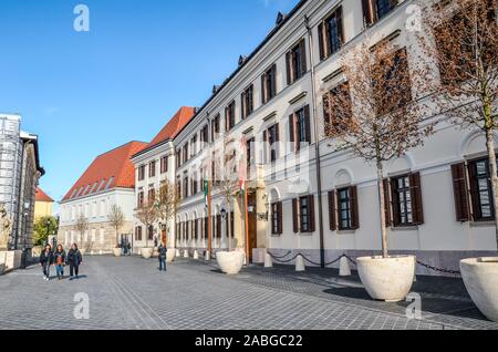 Budapest, Ungarn - Nov 6, 2019: Straße mit Kopfsteinpflaster im Burgviertel mit dem Bau des Gerichtshof Theater von Buda. Das historische Zentrum von Budapest. Die Menschen gehen auf die Straße. Stockfoto