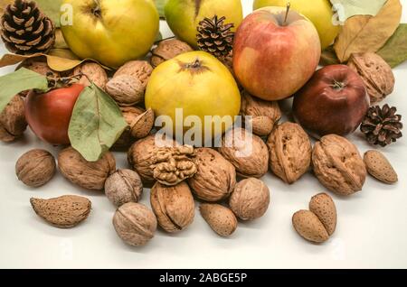 Herbst Ernte von Mandeln mit Walnüssen, reife Äpfel, vergilbte Quitte, Kaki in der Nähe der Kegel und trockenen vergilbte Blätter Stockfoto