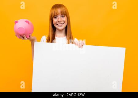 Rothaarige Mädchen mit einem Sparschwein und eine Fahne in der Hand über Gelb bunten Hintergrund Stockfoto