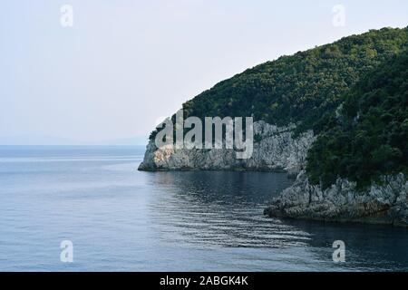 Steile, felsige Ufer, mit dichtem Wald bedeckt, mit dem Wasser der Adria gegen den blauen Himmel gewaschen. Stockfoto