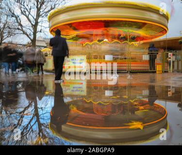 London, Großbritannien. 27. November 2019. Die Leute auf der Southbank sind in Regen Pfützen neben einem bunten Karussell auf der Hauptstadt South Bank wider. PeopleIt wurde überwiegend eine düstere und regnerischen Tag in der Hauptstadt mit schweren Regen und kalten Temperaturen. Credit: Imageplotter/Alamy leben Nachrichten Stockfoto