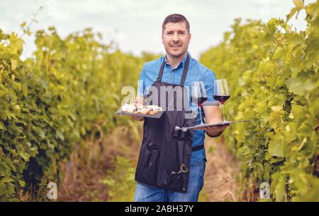 Mann im Weinberg einladende Touristen mit Rotwein und Käse - Weinproben Konzept Stockfoto