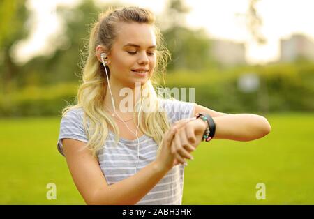 Junge Athlet das Hören von Musik während des Trainings im Park und die Einstellung der Smart watch - junge Frau einstellen Der smartwatch vor Sport in Th Stockfoto