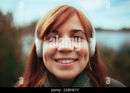 Junge Frau mit einem selfie mit Ihrem Smartphone in der Nähe von einem See und Kopfhörer