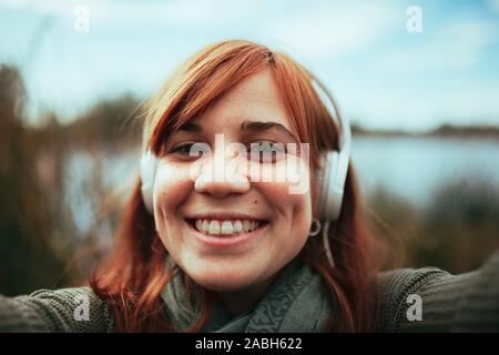 Junge Frau mit einem selfie mit Ihrem Smartphone in der Nähe von einem See und Kopfhörer