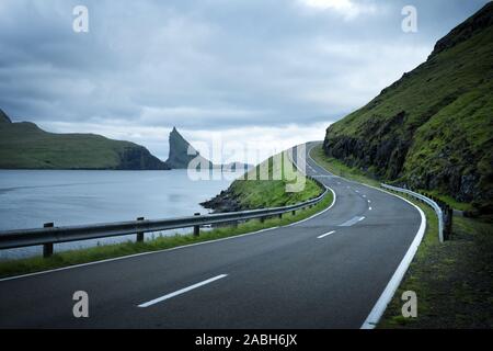 Dramatische Abendlicher Blick von der Straße und der Drangarnir und Tindholmur Felsen im Hintergrund auf der Insel Vagar, Färöer, Dänemark Stockfoto