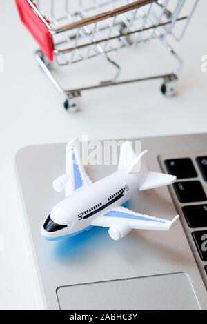 Ein Modellflugzeug steht auf einem Laptop neben einem Trolley. Das Konzept der Kauf von Tickets für einen Flug über das Internet. Vertikale. Stockfoto