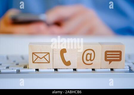 Ein Mann hält ein Smartphone mit seinen Händen, im Vordergrund Es gibt Holz- Würfel mit Buchstaben, E-Mail-, Telefon- und Nachrichtensymbole. Das Konzept der Anzeigen Stockfoto