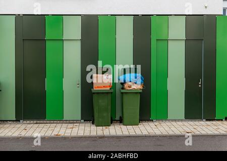 Zwei überfüllte Mülleimer auf eine gestreifte Wand Stockfoto