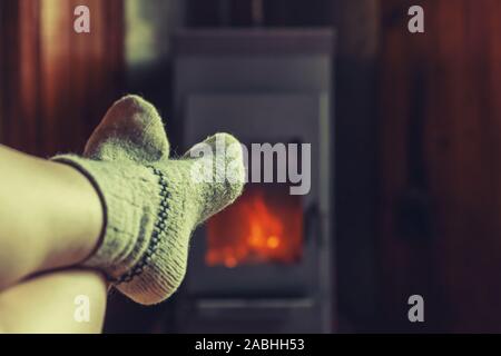 Füße Beine im Winter Kleidung Wolle Socken am Kamin Hintergrund. Frau sitzt zu Hause auf Winter oder Herbst am Abend entspannen und aufwärmen. Winter und Kälte Konzept. Hygge Heiligabend Stockfoto