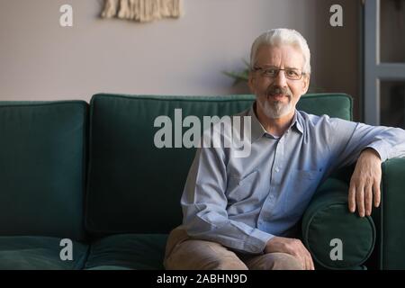 Single gut aussehender älterer Mann saß auf der Couch bei Camera suchen Stockfoto