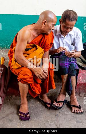 Ein buddhistischer Mönch und lokaler Mann Plaudern auf der Plattform eines Bahnhof, Yangon, Myanmar. Stockfoto