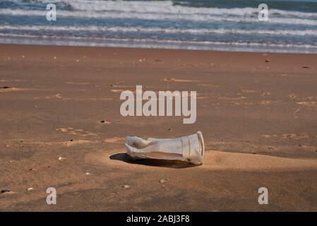 Dieses einzigartige Foto zeigt einen verworfenen Plastikbecher, der vom Meer zum Strand gespült wurde Stockfoto