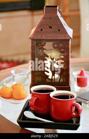 Espresso in festlichem Rot Becher mit Kupfer Laterne und Mandarine Orangen im Hintergrund. Vertikale Format. Hygge komfort Konzept. Stockfoto