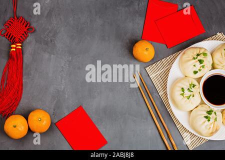 Das chinesische Neujahr Dekoration mit Knödel, Mandarinen, Sojasauce, Essstäbchen, rote Umschläge auf grauem Hintergrund. Vorlage. Happy Chinese New Year 2020 Stockfoto