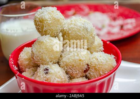 Schön gestapelt coconut Rava ladoos in einem roten Schüssel mit Milch und Kokosnuss Pulver in den Hintergrund. Stockfoto