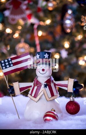 Amerikanische Schneemann ist in patriotischen Rot und Blau gekleidet und mit einer Fahne vor dem Weihnachtsbaum gestellt Stockfoto