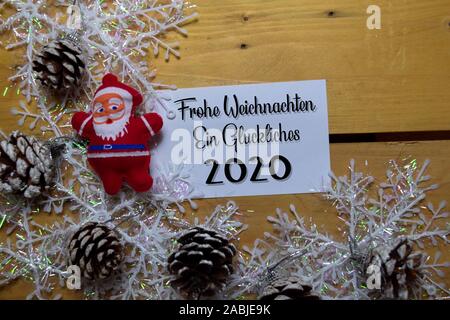 Frohe Weihnachten und ein GLUCKLICHES 2020 Schreiben auf weißem Papier mit Holz- Hintergrund. Es bedeutet, frohe Weihnachten. Rahmen der Weihnachtsdekoration. Stockfoto