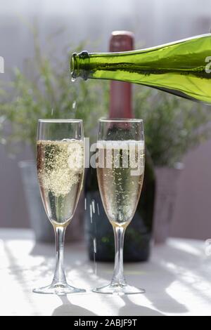 Mit einem luxuriösen sprudelnder Champagner in zwei Glas Gläser, mit einem grünen Flasche Champagner im Hintergrund, konzentrieren. Hochzeit und Feier Stockfoto