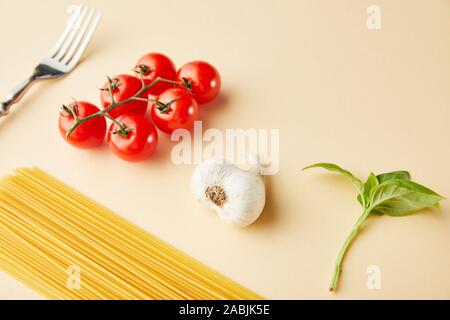 Rohe Spaghetti, Knoblauch, Tomaten, Basilikum und Gabel auf gelbem Hintergrund Stockfoto