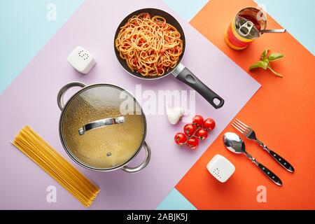 Flach mit leckeren Spaghetti mit Tomatensauce Zutaten und Küchengeräte auf rote, blaue und violette Hintergrund Stockfoto