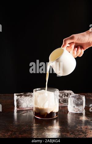 7/8-Ansicht von Frau brütete Milch in Glas mit Eiswürfeln isoliert auf Schwarz Stockfoto