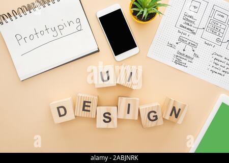 Blick von oben auf die Gadgets in der Nähe von Holz- Bausteine mit ui design Schriftzug, website design Vorlage, Notebook mit prototyping Schriftzug und grüne Pflanze auf beige Stockfoto