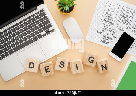 Blick von oben auf die Gadgets in der Nähe von Holz- Bausteine mit Design Schriftzug, website design Template und grüne Pflanze auf beigen Hintergrund Stockfoto