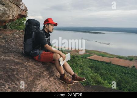 Mann Reisender mit Rucksack sitzt am Rande der Klippe, an der Spitze der Rock Mountain Stockfoto