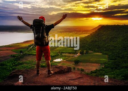 Fröhliche Wanderer mann Geste erhobenen Armen am Rand der Klippe, auf der Spitze des Felsens Berge bei Sonnenuntergang Stockfoto