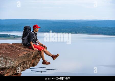 Mann Reisender mit Rucksack sitzt am Rande der Klippe, an der Spitze der Rock Mountain Stockfoto