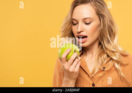 Junge Frau mit Zahnspangen beißen green apple isoliert auf Gelb Stockfoto