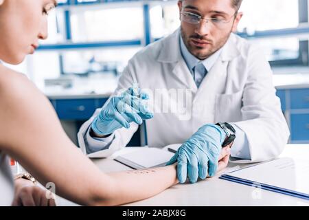 Selektiver Fokus der Allergologe in Latex Handschuhe halten Sie die Spritze in der Nähe der attraktiven Frau in der Klinik Stockfoto