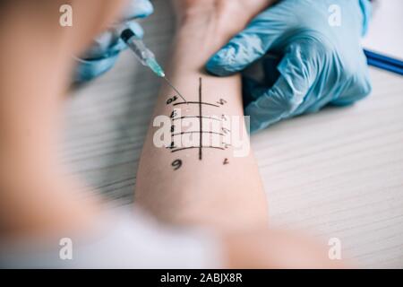 7/8-Ansicht von allergist halten Sie die Spritze in der Nähe der Frau beim Allergietest in Klinik Stockfoto