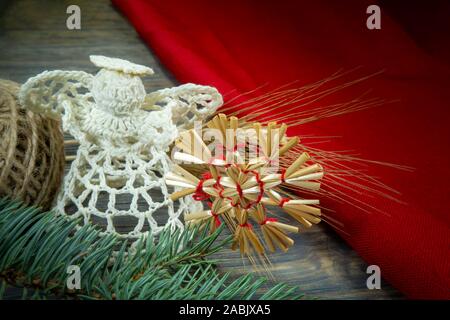 Weihnachten Hintergrund mit handgefertigten Ornamenten einschließlich der Engel gehäkelt Gewinde und einem STROHHALM Stern mit rotem Garn gebunden über einen rustikalen, mit Holz backgro Stockfoto