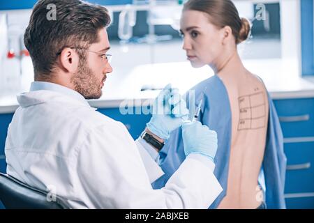 Selektiver Fokus der stattlichen allergist halten Sie die Spritze in der Nähe von Patienten mit Buchstaben auf markierten zurück Stockfoto