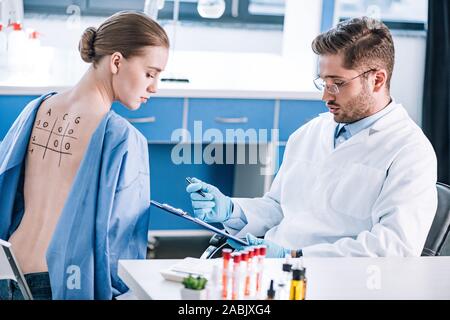 Selektiver Fokus der stattlichen allergist Holding Zwischenablage in der Nähe von Frau mit Zurück gekennzeichnet Stockfoto