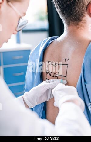 7/8-Ansicht von allergist in Latex Handschuhe halten Sie die Spritze in der Nähe der Mann mit Zurück gekennzeichnet Stockfoto