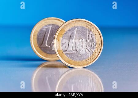 Zwei ständige 1 Euro Münzen auf einem blauen reflektierenden Hintergrund mit Reflexionen in der Münzen verkratzt Stockfoto
